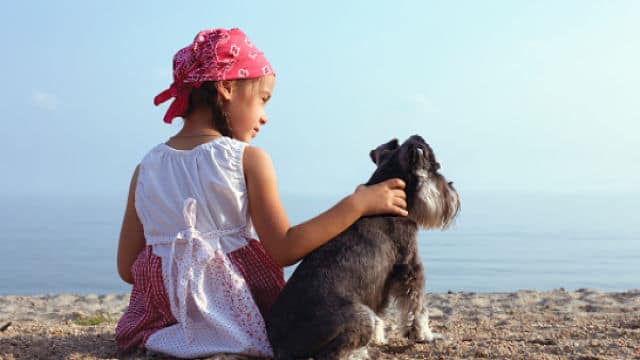 girl sitting at the beach next to a dog