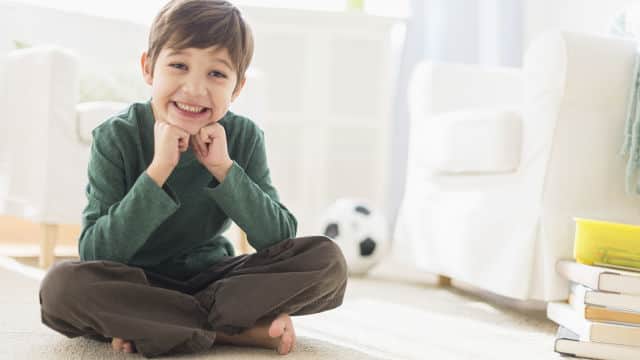 A boy smiling brightly sitting down on the floor