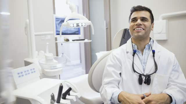 Dentista sonriente de mediana edad en consultorio odontológico