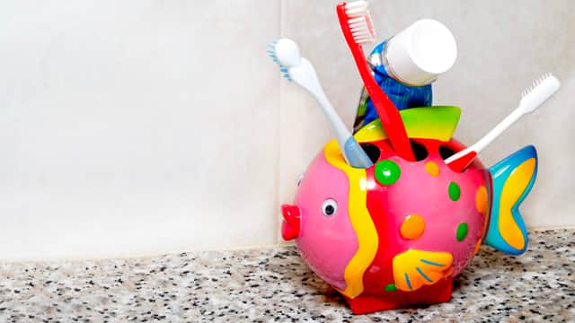 Children's, fish-shaped toothbrush and toothpaste holder sitting on a counter.