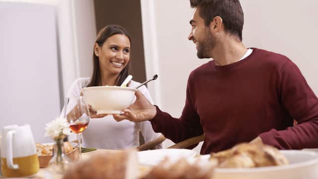 a woman smiling while passing a salad bowl to a man