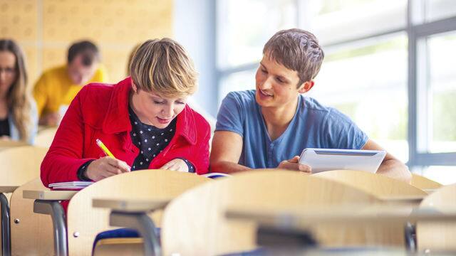 a man and a woman sitting down in a classroom studying