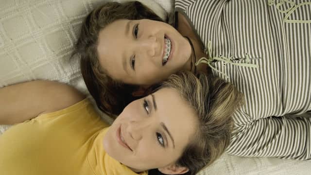 Smiling girl with dental braces lying head-to-head with another girl