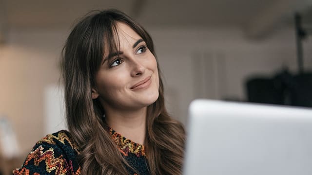 Smiling brown haired woman using a laptop to figure "out what is a dentigerous cyst?"