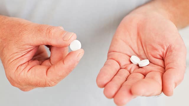 Hands holding and inspecting white rounded pills.