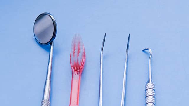Picture of tooth extraction concept with a set of stainless steel dental tools. Set of stainless steel dental tools and one red tooth brush.