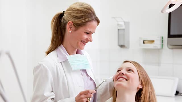 Smiling female dentist holding a dental tool in white lab coat with patient