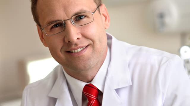 Smiling male Dentist with glasses sporting a red tie.