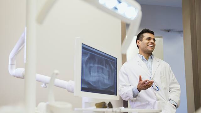Dentist laughing in doorway of office Happy Dentist explaining to unseen person what Cerec is.