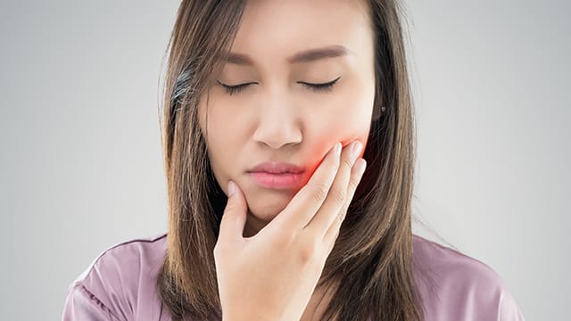 Brown colored hair woman, touching her cheek, feeling the pain of gums burned.