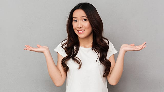 Young woman in white top against gray background shrugging, wondering how does one cope with gag reflexes?!