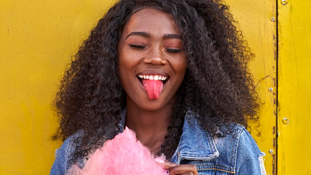 Smiling young woman with pink candy floss sticking out tongue.