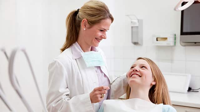 A female dentist is checking on a female patient who is sitting on a dental chair 