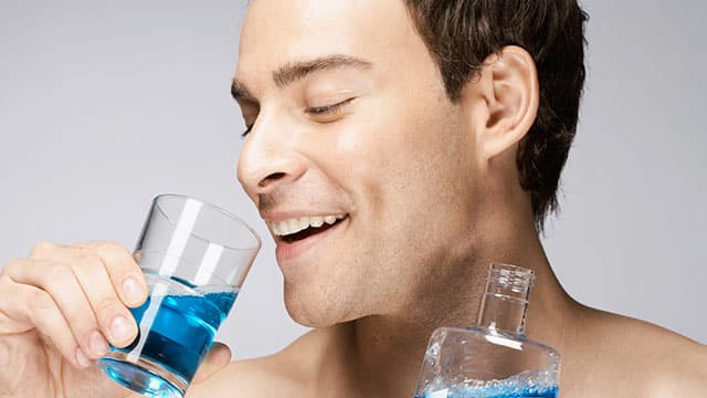 A man using a mouthwash in a bathroom