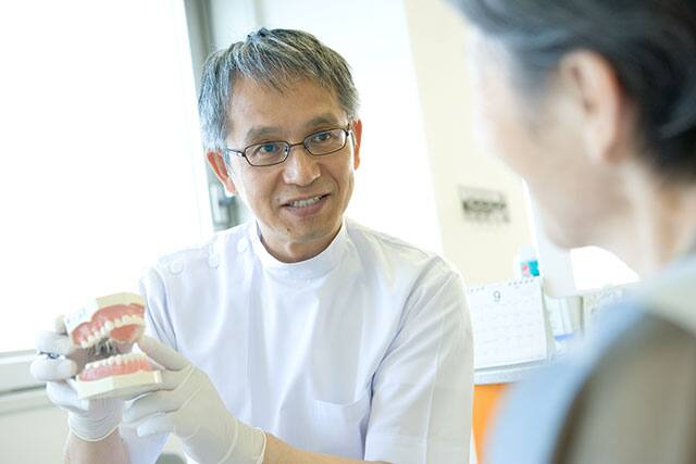 A dentist holding a mouth model is talking to a female patient