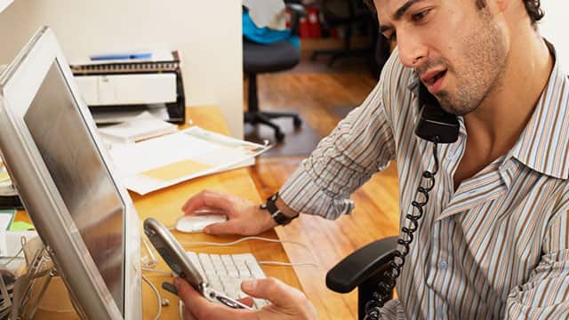 A man using his computer and talking on a phone A man using his computer and talking on a phone