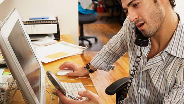 A man using his computer and talking on a phone