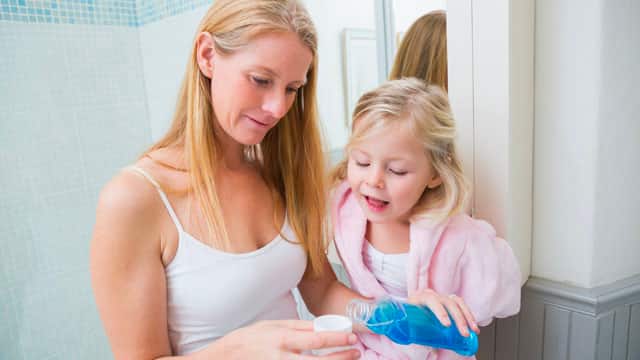 A mother and a daughter pouring mouthwash. A mother and a daughter pouring mouthwash.