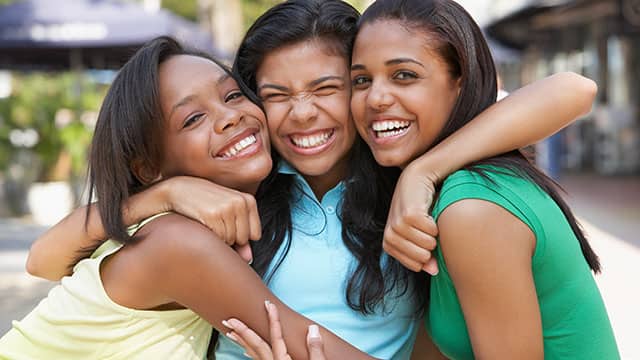 three young girls are hugging and laughing together