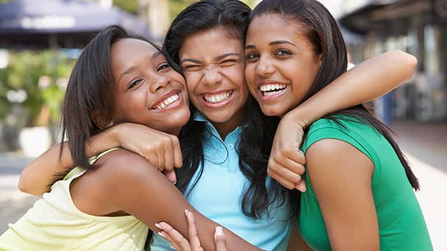 three young girls are hugging and laughing together three young girls are hugging and laughing together