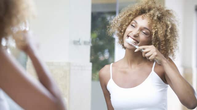 a woman brushing her teeth with Colgate toothbrush in front of a mirror