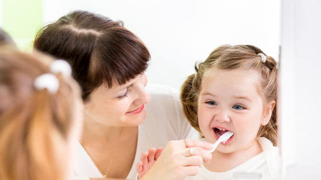 Madre cepillando los dientes a su hija