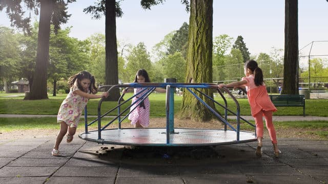 three girls running around a merry go round at the playground