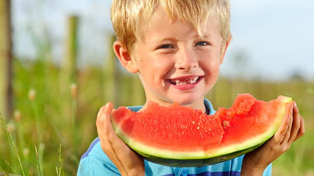 A kid smiling and eating a watermelon