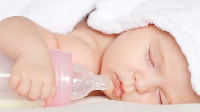 A close up of the baby lying on his stomach and holding a milk bottle