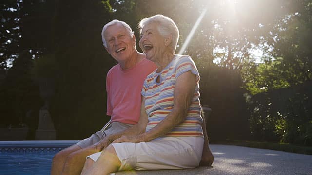 an elderly couple smiling sitting by the pool