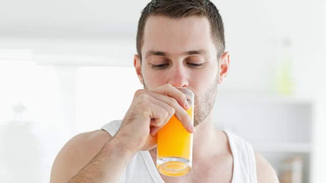 Man with beard in undershirt drinking orange juice