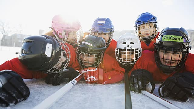 Kids wearing ice hockey gear lying on the ice rink