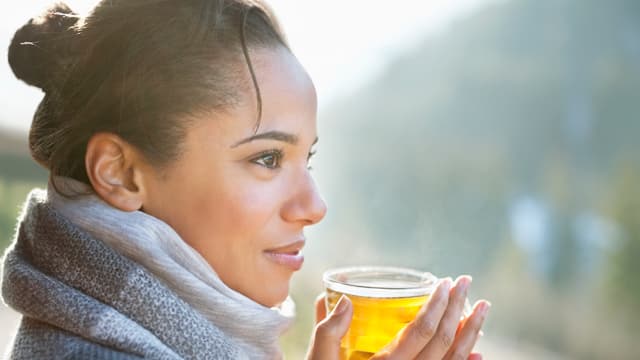 A woman in a scarf drinking hot tea outside