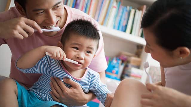 parents are teaching their toddler to brush teeth