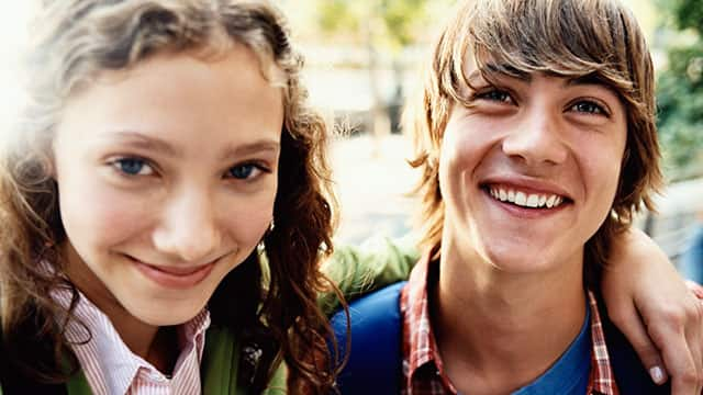 Teenage girl stands smiling with her arm around a friend