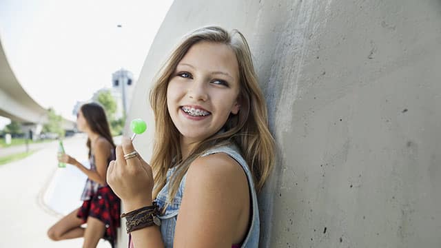 Teenage girl smiling with braces outside while eating a lollipop