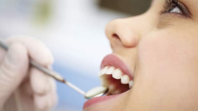 A close up of woman's face being checked by a dentist