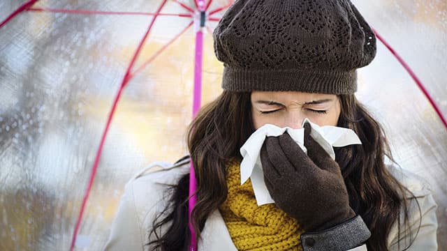 A woman sneezing outside