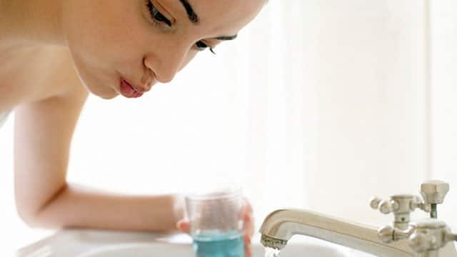 A woman is using a mouthwash over the sink