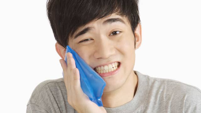 A young Asian man is holding an ice pack to his cheek