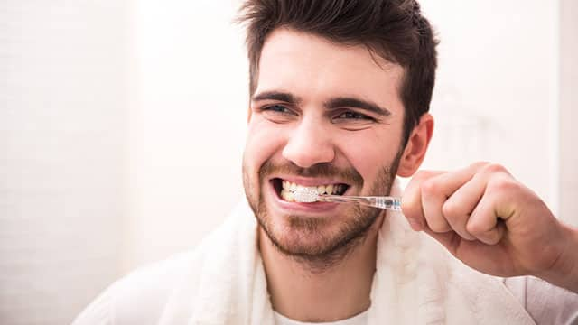 Young man brushing his teeth while looking into a mirror