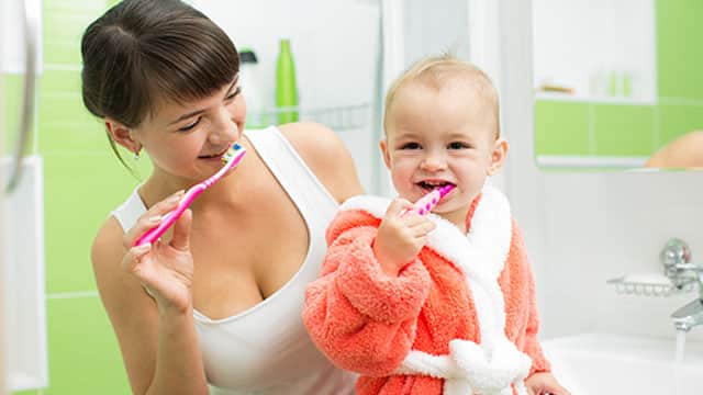 A mom and a baby brushing their teeth