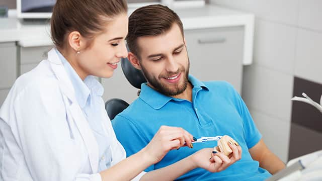 Dental hygienist is showing a patient how to brush teeth