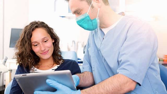 a dentist wearing a mask showing tablet to a patient