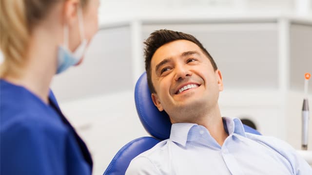 A female dentist talks with a happy male patient sitting in dental chair