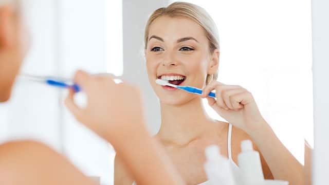 A woman brushing her teeth in front of the bathroom mirror