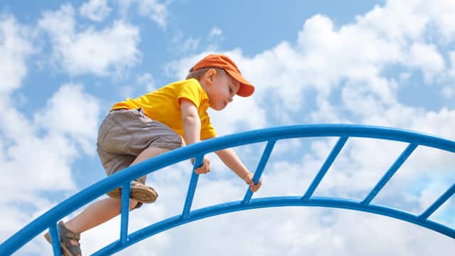 Young boy in orange hat and yellow shirt climbing on top of monkey bars