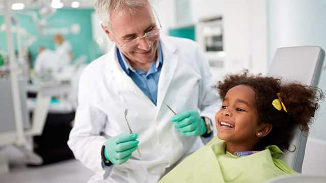 A happy kid in dental chair and a dentist holding tools 