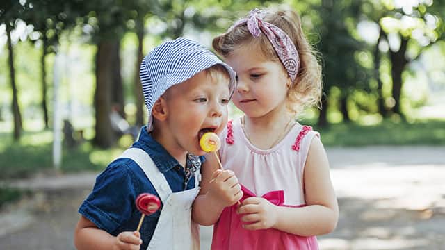 Two happy children tasting lollipops outside in the park