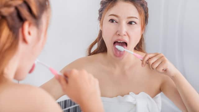 Young woman in a towel brushing her tongue in a bathroom mirror